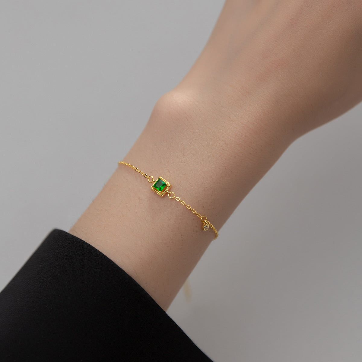 A close-up of a 925 sterling silver bracelet, plated in 18k gold, featuring a brilliant green square emerald zircon stone.