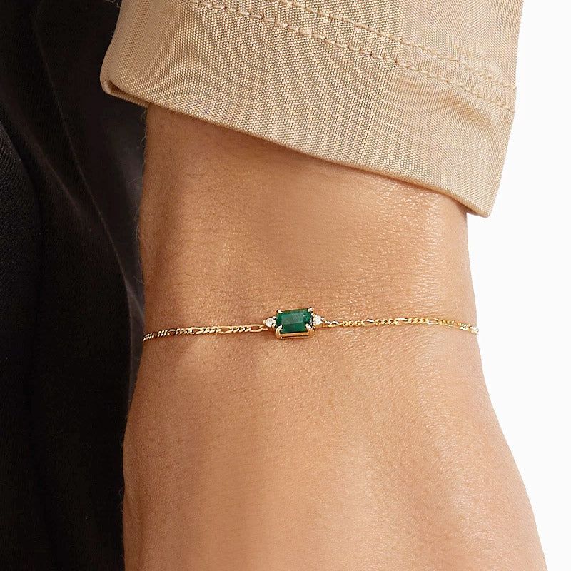 Una vista detallada de una pulsera de cadena Figaro de plata esterlina 925 chapada en oro, centrada con una brillante zirconia rectangular verde esmeralda.