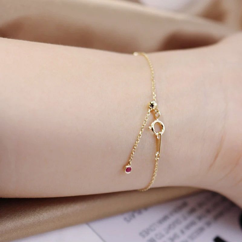 Primo piano di un bracciale a catena in argento sterling 925 con finitura dorata, caratterizzato da un vivace ciondolo rotondo in pietra preziosa rossa.