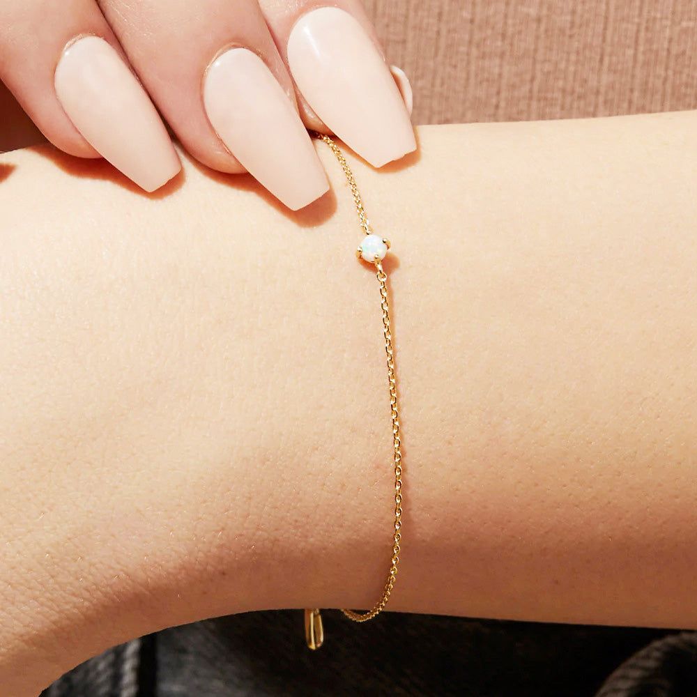 Un delicato bracciale a catena in argento sterling 925 con un singolo pendente in opale in finitura dorata, indossato su un polso per mostrare il suo design elegante.