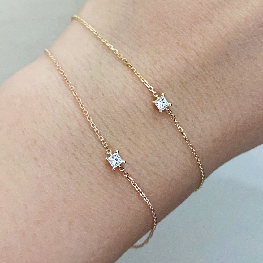 Un set di due bracciali minimalisti impilabili in argento sterling 925, ciascuno con una singola pietra quadrata in zirconia cubica, esposti su uno sfondo neutro.