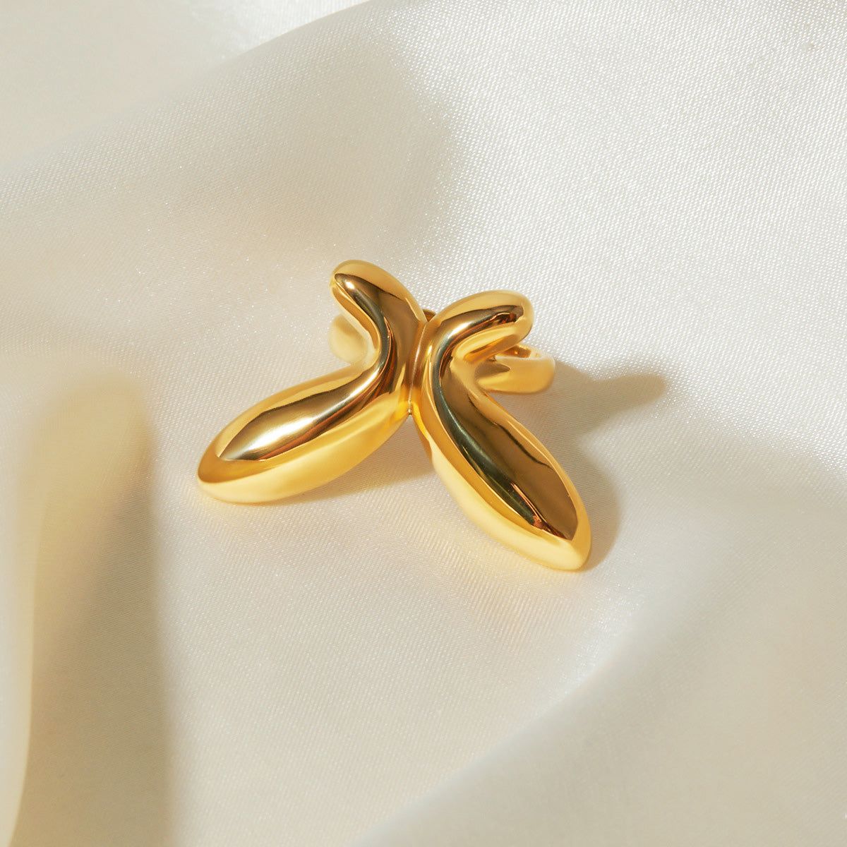 Um conjunto de cinco anéis ajustáveis abertos banhados a ouro em aço inoxidável, apresentando designs geométricos de curvas e borboletas, exibidos sobre um fundo de tecido branco.