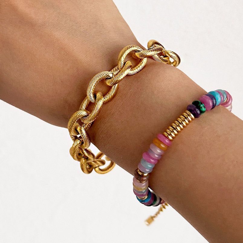 Een stijlvolle set van vijf roestvrijstalen armbanden met een gouden afwerking, met een mix van brede schakels en gedraaide touwontwerpen met sluitingen, gerangschikt op een effen achtergrond.