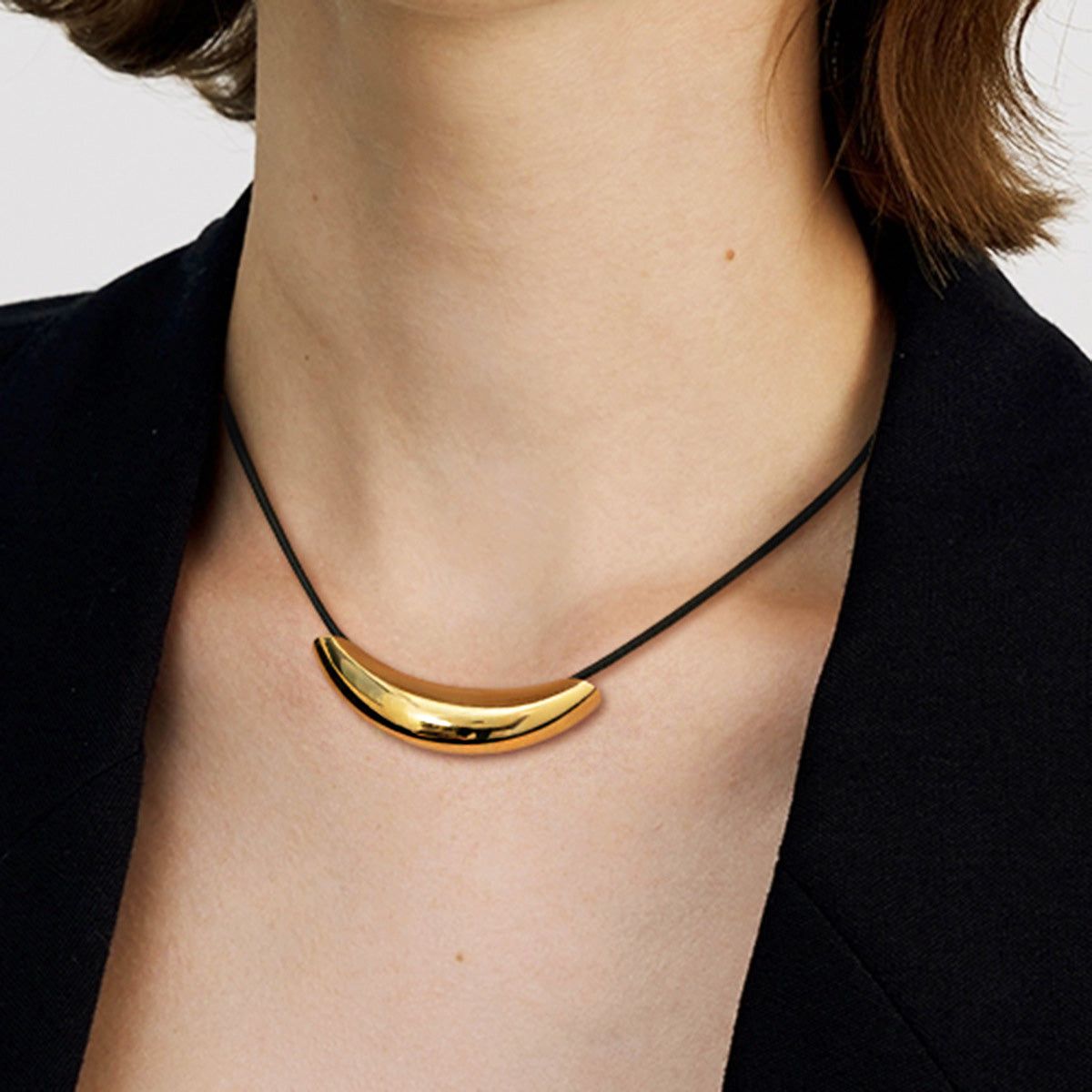 En kvinna som bär ett minimalistiskt halsband med guldfinish i rostfritt stål och en svart läderrem.
