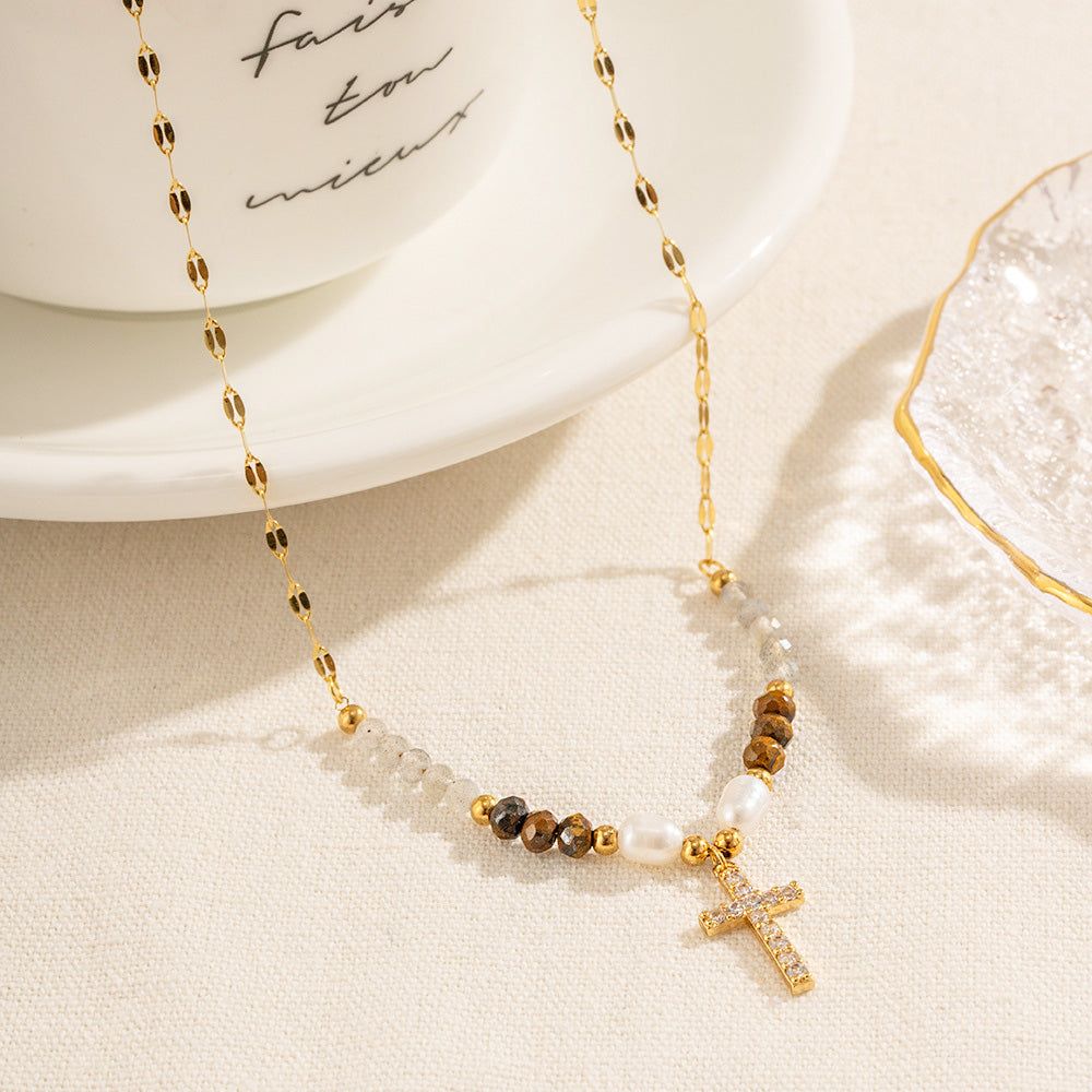 Gros plan d'un collier en acier inoxydable doré avec une chaîne perlée délicate et un pendentif croix en zircon cubique, présenté sur un fond blanc propre.