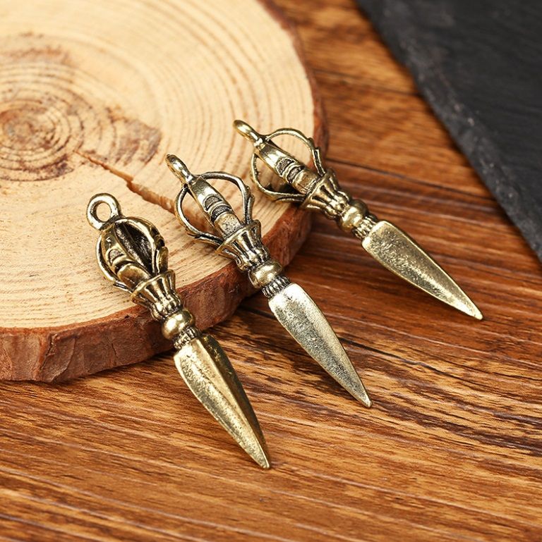 Un set di tre ciondoli strumentali patriarcali esoterici tibetani antichi personalizzati, stilizzati come orecchini a forma di pugnale placcati in oro, esposti su una superficie di legno.