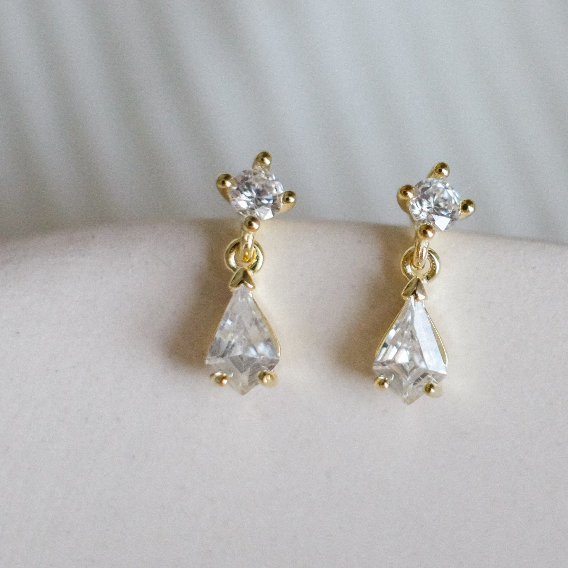 Un paio di orecchini a goccia d'acqua in cristallo in argento sterling 925 con finitura dorata, che mostrano un design delicato con gemme chiare rotonde e a goccia.