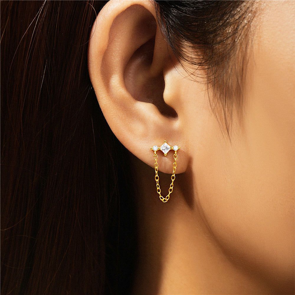 Un primo piano di una donna che indossa un delicato orecchino a frangia placcato oro in argento sterling 925 con un elemento a catena in zirconio scintillante.
