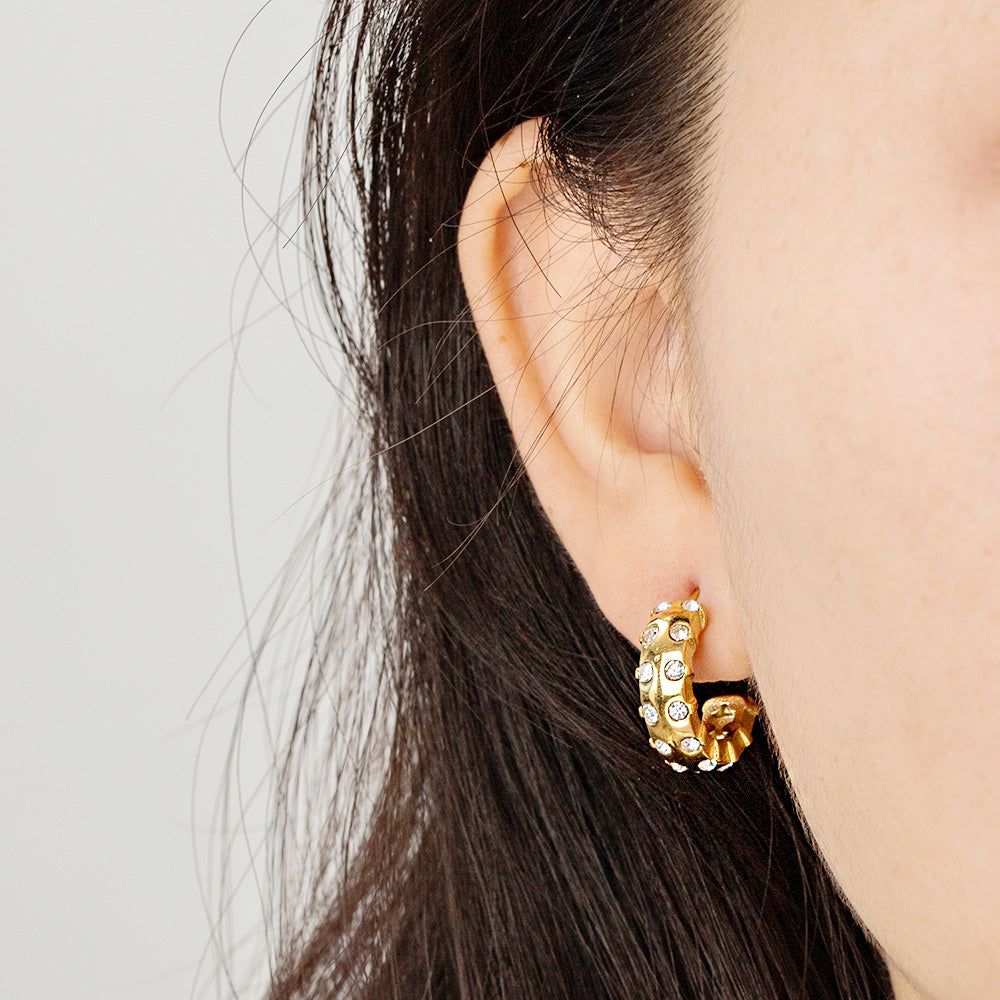 Un primer plano de una mujer que lleva el pendiente de zirconia blanca en forma de C con incrustaciones de oro en acero inoxidable, mostrando su elegante diseño y brillo.