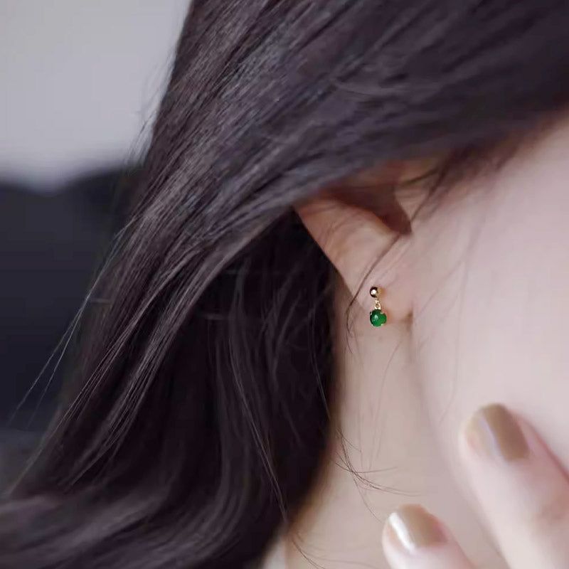 En närbild av en kvinna som bär ett klassiskt, minimalistiskt litet jadeörhänge i 925 sterling silver, som visar dess eleganta design och livfulla gröna sten.