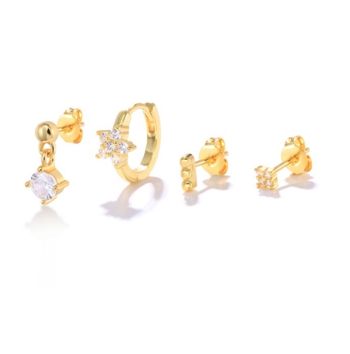 Un set di quattro diversi orecchini huggie a cerchio in oro, ciascuno adornato con scintillanti pietre di zirconia cubica bianca, esposti su una superficie bianca.