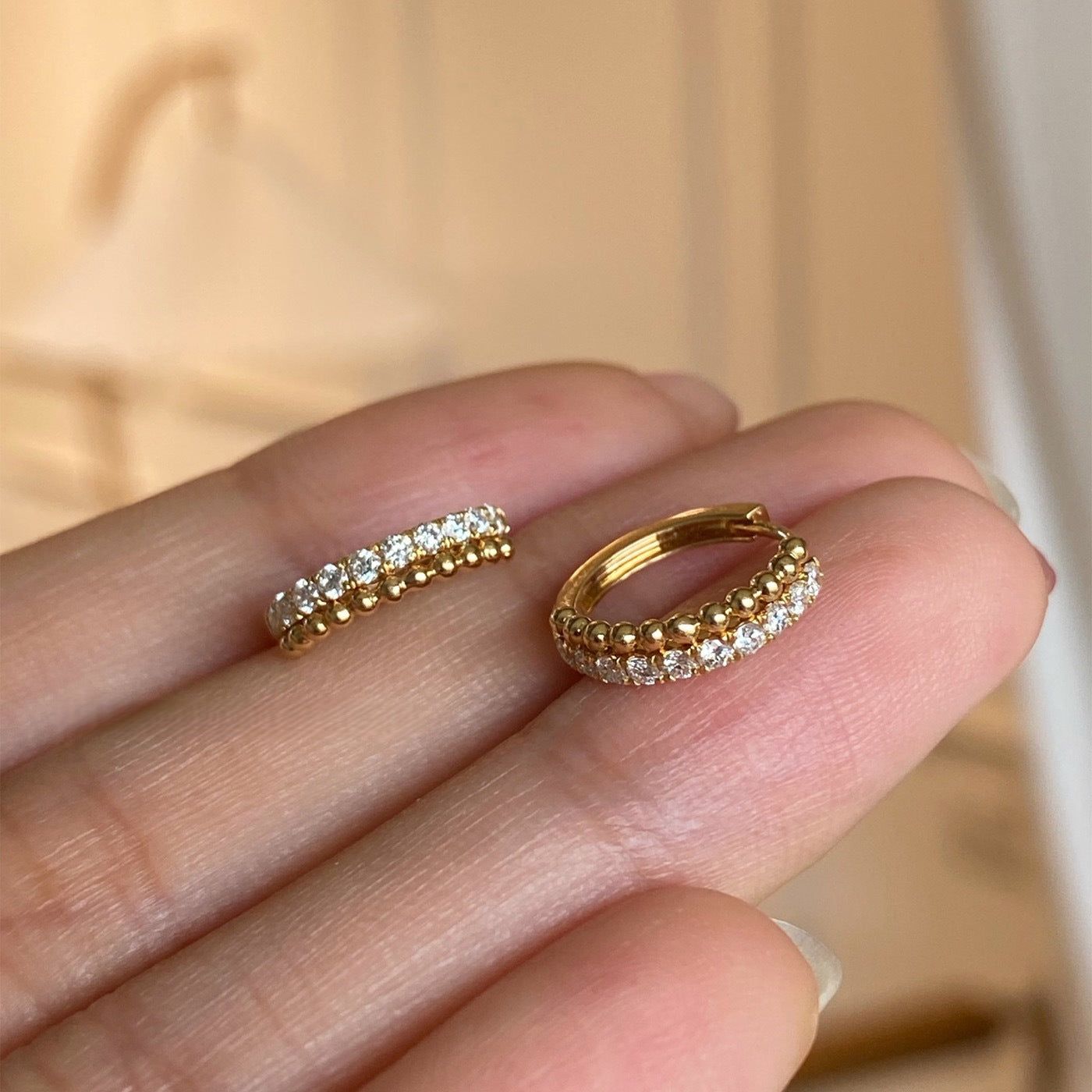 Una vista ravvicinata di un paio di orecchini huggie a cerchio in argento sterling 925 placcati in oro 18k, con una fila di brillanti gemme di zirconia cubica trasparente.