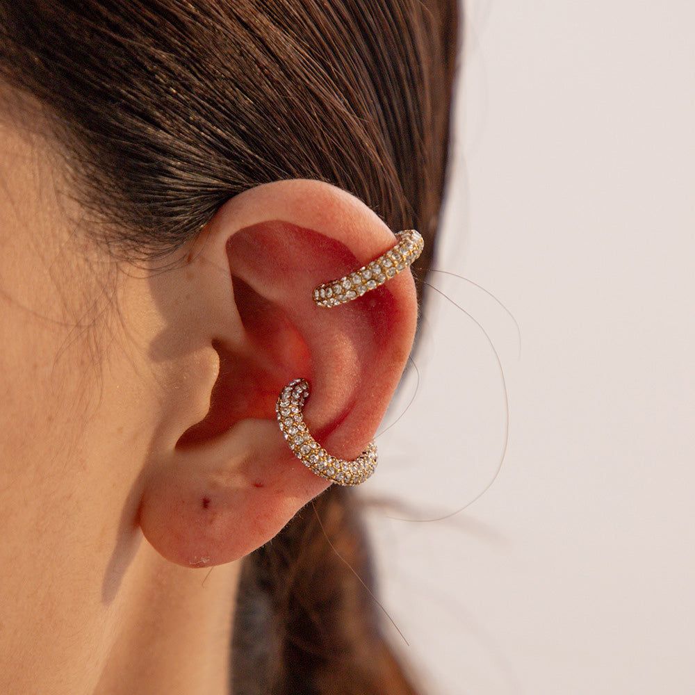 Een close-up van twee goudkleurige roestvrijstalen oorclip oorbellen versierd met sprankelende witte rhinestones, die hun elegante ontwerp toont.