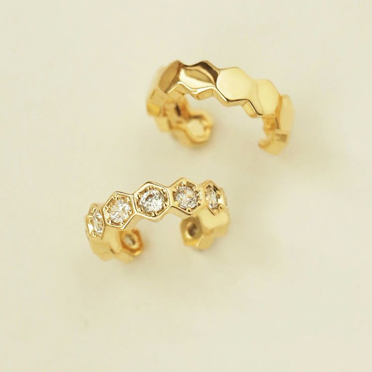 Een paar vergulde 925 zilveren mismatched oorcuffs, de ene met een gladde afwerking en de andere versierd met sprankelende edelstenen, op een witte achtergrond.