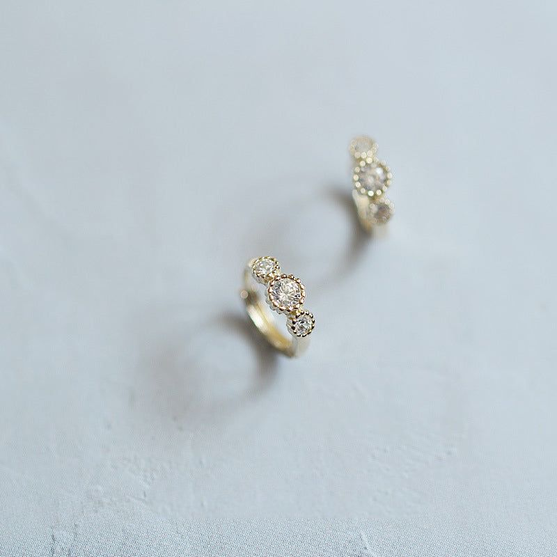 A close-up view of the 925 sterling silver gold-plated hoop huggie earrings, each featuring three sparkling clear zirconia gemstones.