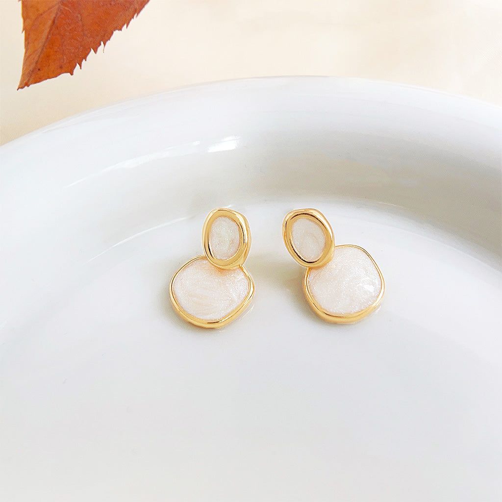 A pair of 14k gold-plated circle drop earrings with cream-white enamel, displayed on a white surface.