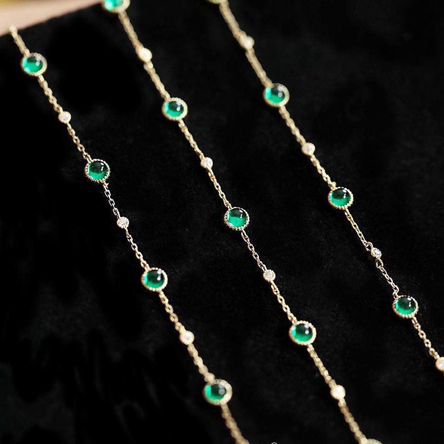 Un conjunto al por mayor de pulseras de cadena de plata esterlina 925 con piedras de esmeralda y circonio, elegantemente exhibidas en un soporte de terciopelo negro.