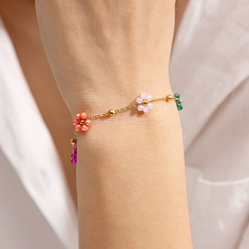 En närbild av ett guldigt armband i rostfritt stål från setet, med delikata blomstercharmar och färgglada ädelstenpärlor.