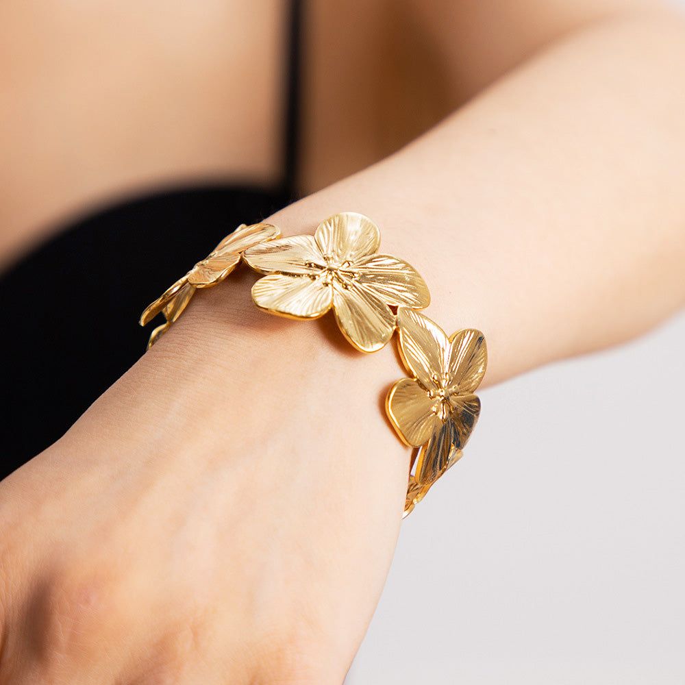 Das Handgelenk einer Frau, geschmückt mit dem eleganten breiten Armreif aus Edelstahl mit goldenen Blumen, der sein filigranes Blumendesign präsentiert.