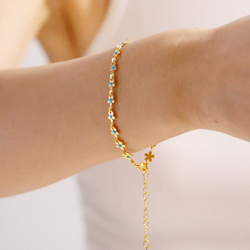 Das Handgelenk einer Frau, geschmückt mit dem Armband-Set aus Edelstahl im Boho-Stil, das zarte Blumenanhänger aus blauer Emaille enthält.