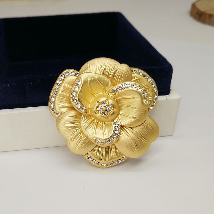 ヴィンテージのマットゴールドの葉と椿のブローチのクローズアップで、複雑な花のデザインときらめく中央のラインストーンを強調しています。