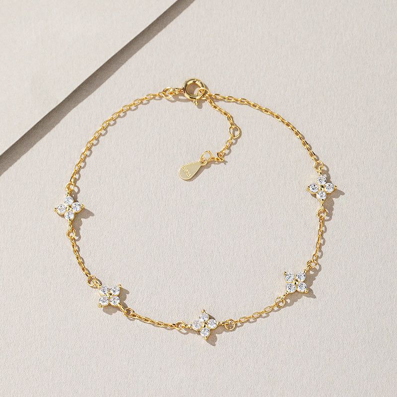 A close-up of a 925 sterling silver, 18k gold plated bracelet from a set, featuring a four-leaf clover charm embellished with sparkling white zircon stones.