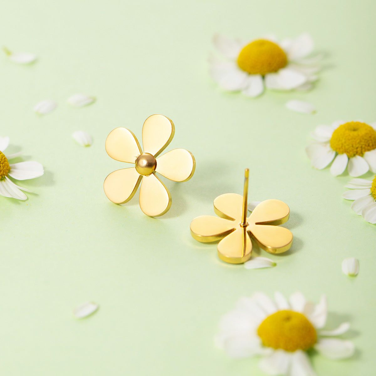 A pair of gold stainless steel daisy flower stud earrings displayed on a white stand, showcasing their delicate petal design.
