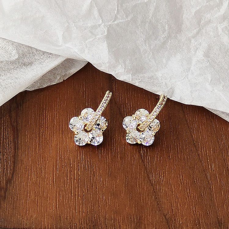 きれいな白い背景に、きらめく透明なジルコンクリスタルをあしらった金メッキの花のスタッドイヤリングのペア。