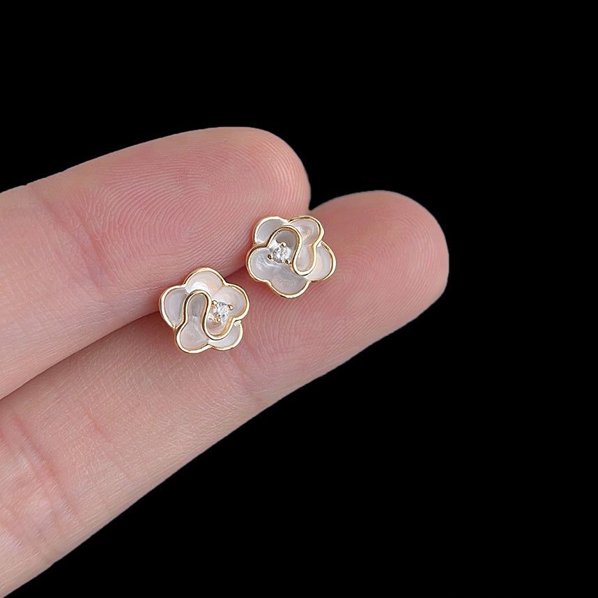 Gros plan sur une boucle d'oreille clou plaquée or 14 carats avec un design de fleur en émail blanc et un zircon scintillant au centre.