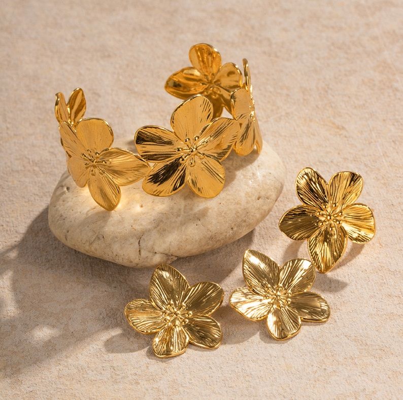 Elegant Stainless Steel Flower Jewelry Set with gold plating, featuring matching earrings and bracelet displayed on a decorative stone.
