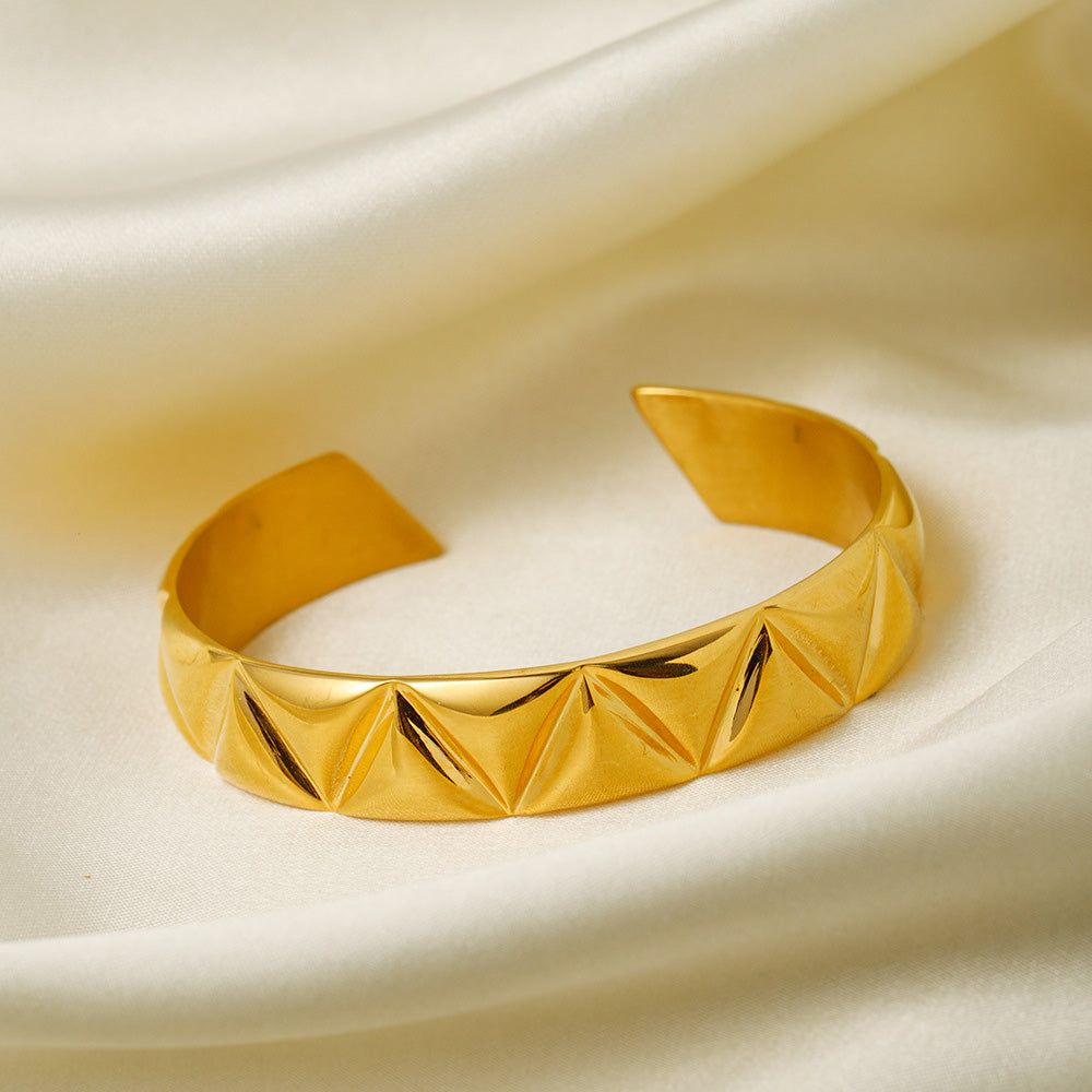 En närbild av det 18K guldpläterade armbandet i rostfritt stål, med en detaljerad geometrisk triangelyta.