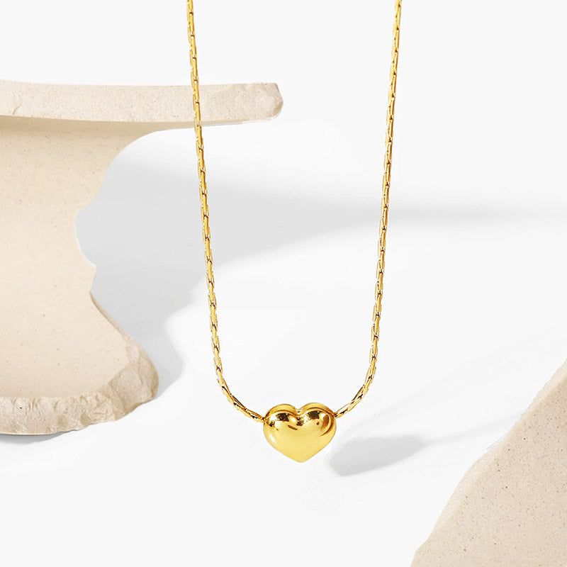 Ett delikat halsband med guldfinish i form av ett hjärta, tillverkat av allergivänligt rostfritt stål, visat på en neutral bakgrund.