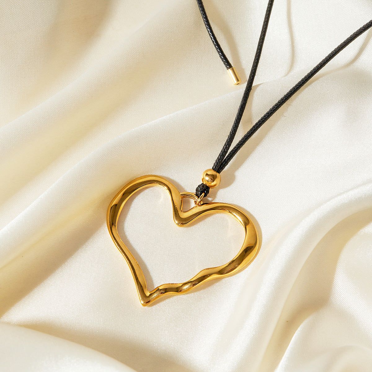 En närbild av guld rostfritt stål ihåligt hjärtanhänge på ett svart läderhalsband, del av ett set om 5.