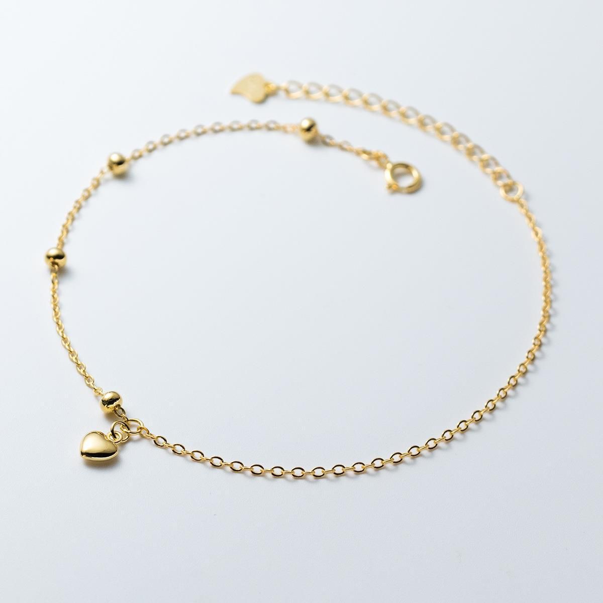 A delicate 925 sterling silver bracelet plated in 18K gold, featuring a mini heart charm and round ball beads on a white background.