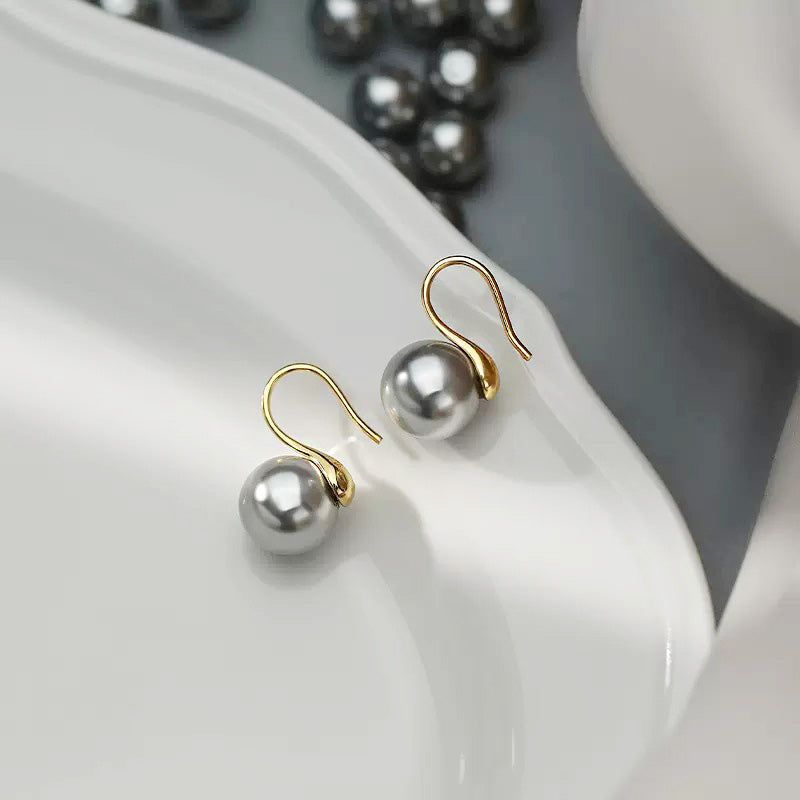 Un primo piano di un singolo orecchino di perla grigia in argento sterling 925 con un gancio francese in oro lucido, che mostra il suo design classico ed elegante.