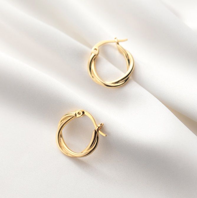Un paio di eleganti orecchini a cerchio attorcigliato in argento sterling 925 con finitura dorata, appoggiati su uno sfondo di satin bianco per evidenziare la loro lucentezza.