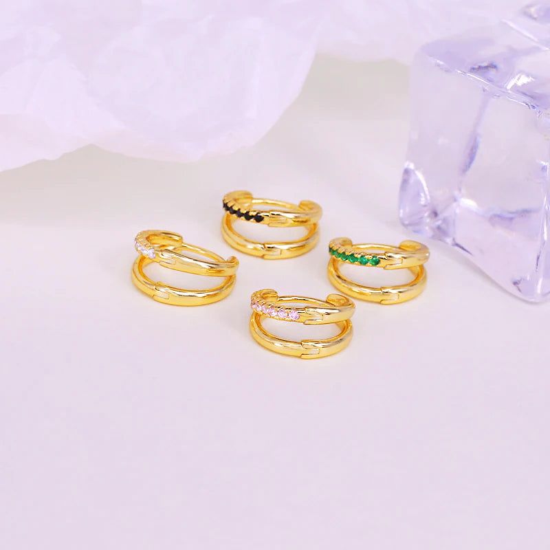 Una collezione di orecchini a cerchio in cartilagine a doppio cerchio in argento sterling 925 con finitura dorata, che mostra varie opzioni di colore delle pietre tra cui bianco, nero, rosa e verde.