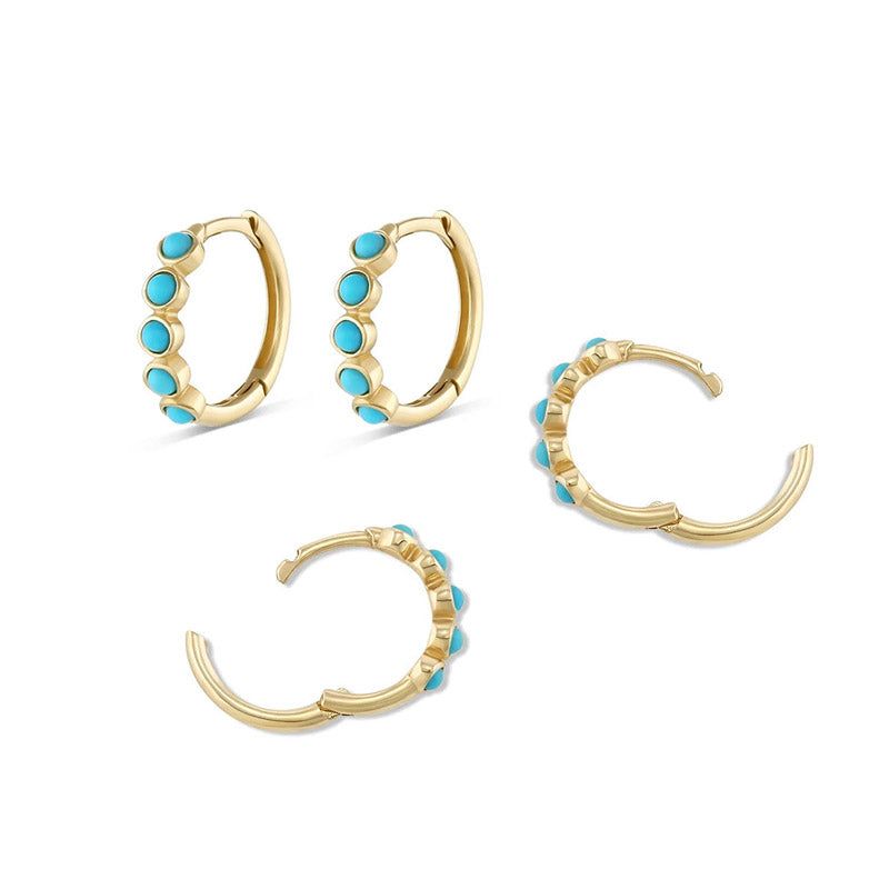 Une paire de boucles d'oreilles huggie classiques en argent sterling 925 avec des pierres turquoises vibrantes, présentées sur un fond blanc.