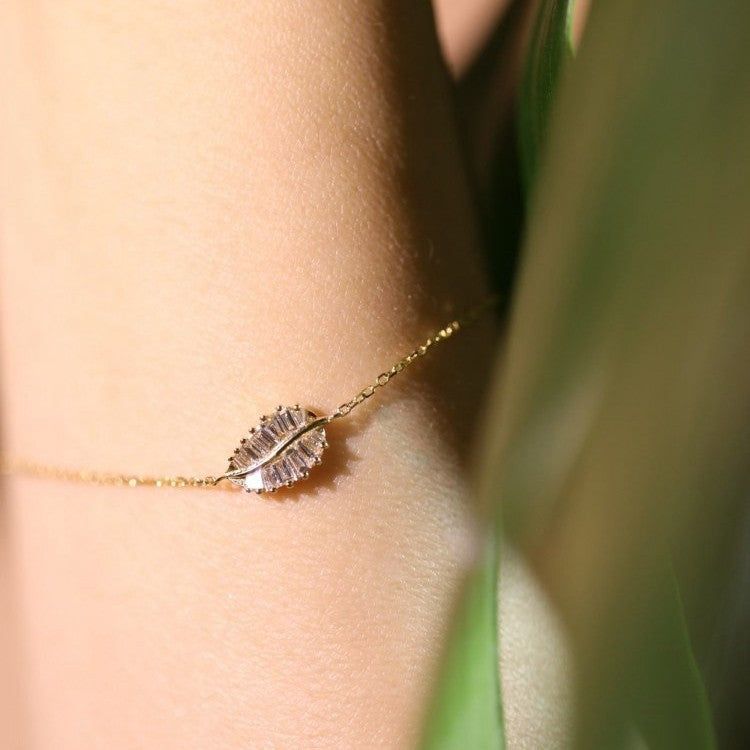 A close-up of an elegant 14K gold-plated sterling silver bracelet featuring a leaf-shaped pendant set with sparkling cubic zirconia stones.