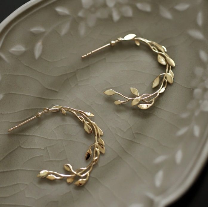 Un paio di orecchini a cerchio fogliare in argento sterling 925 con placcatura in oro, esposti su un piatto decorativo per mostrare il design intricato del ramo fogliare e i dettagli in zirconia cubica.