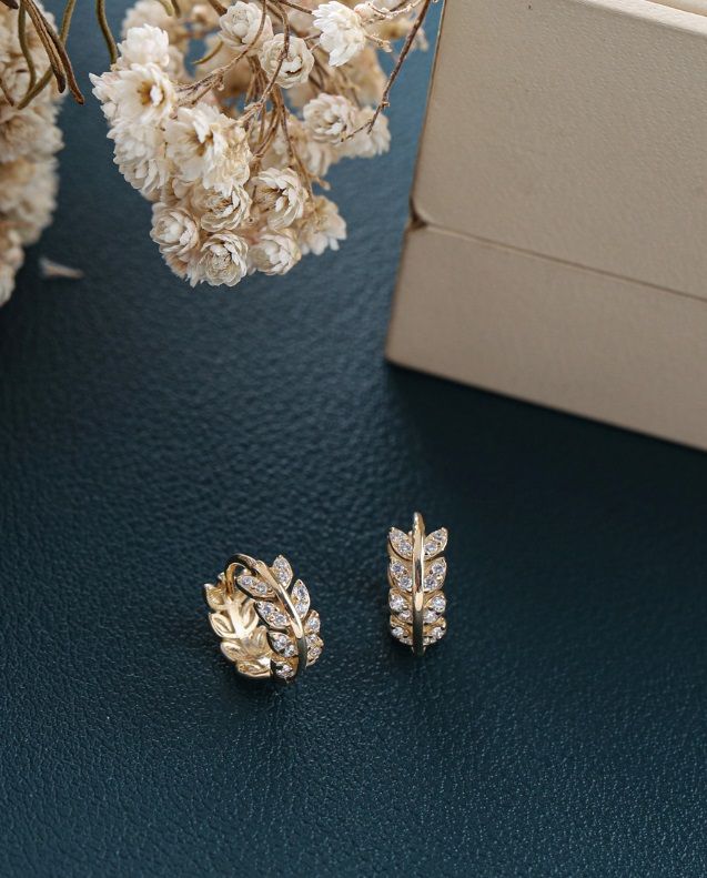 Primo piano degli orecchini a foglia a stella in argento sterling 925, che mostrano il design intricati delle foglie, la placcatura in oro e le brillanti pietre in zirconia cubica.