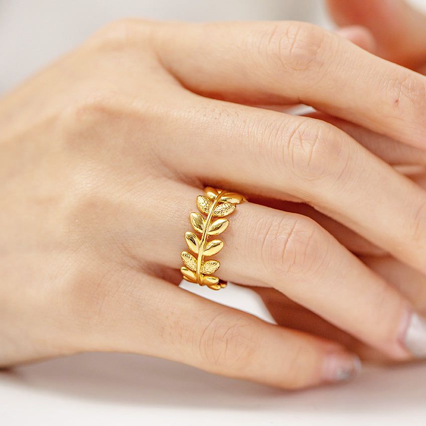 A close-up of a hand wearing the elegant stainless steel olive branch leaf ring with a beautiful gold finish, showcasing its adjustable open design.