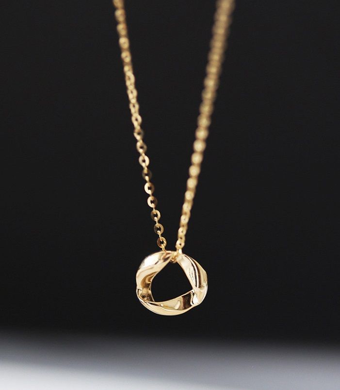 Un collar redondo de plata esterlina 925 con un distintivo colgante circular bañado en oro, mostrado contra un fondo neutro.