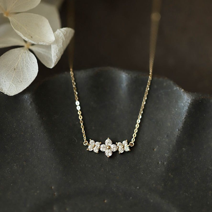 Un delicado collar de plata esterlina 925 con acabado dorado, que presenta un dulce colgante de tres flores con piedras de zirconia brillantes.