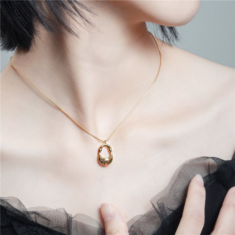 Una mujer que lleva un delicado collar de acero inoxidable en tono dorado con un colgante geométrico ovalado hueco, mostrando su diseño elegante.