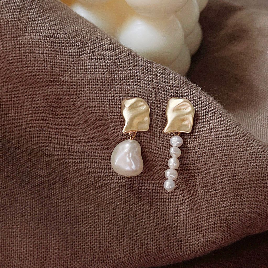 A pair of asymmetrical gold-plated earrings with irregular baroque freshwater pearl pendants, showcasing their unique design.