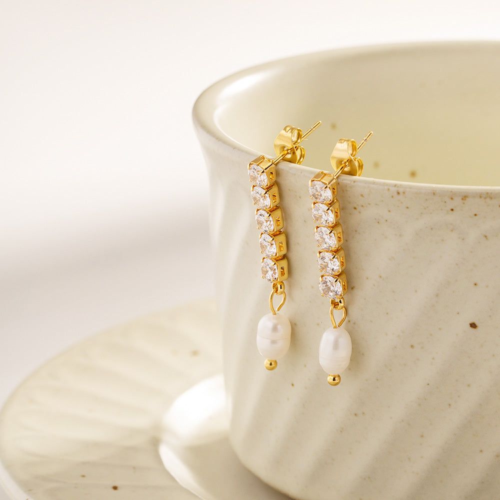 Een paar elegante roestvrijstalen franje hang oorbellen met glanzende zoetwaterparels en sprankelende cubic zirconia stenen, weergegeven op een schone, minimalistische achtergrond.