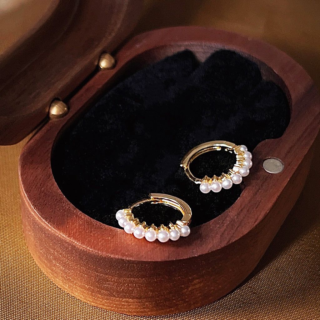 A set of five 14k gold-plated pearl hoop huggie earrings displayed in a black velvet-lined wooden box.