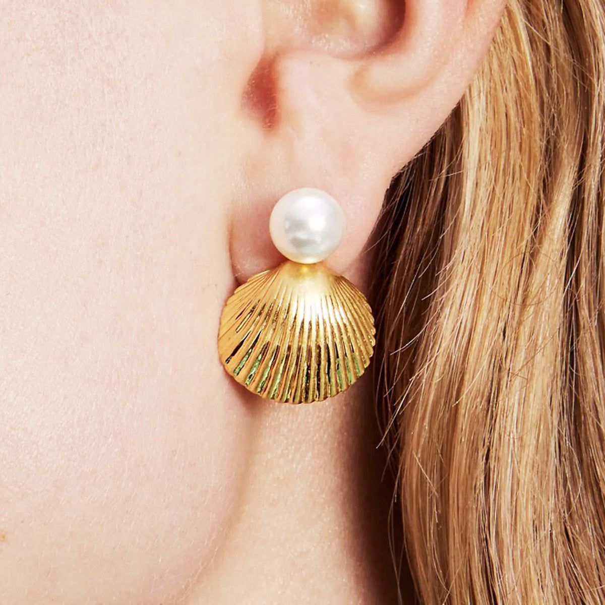 Un primer plano de un arete de perla única en forma de concha de oro de acero inoxidable, mostrando su diseño detallado y acabado brillante.