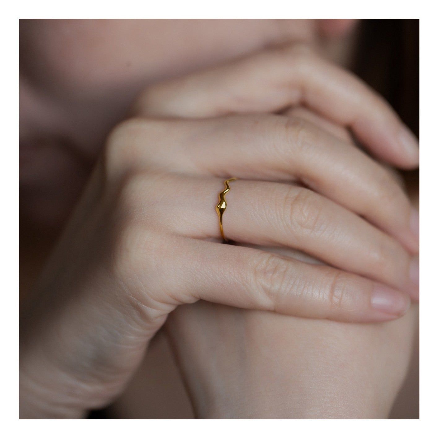 Close-up van een minimalistische 18K vergulde golvende bandring met een druppel detail, gedragen op de vinger van een vrouw om het elegante ontwerp te tonen.